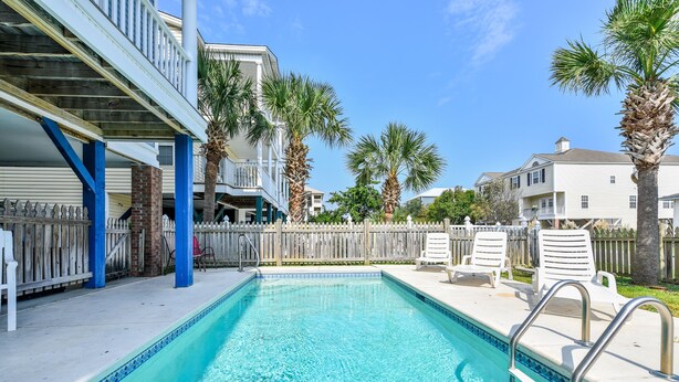A swimming pool with a wooden deck, palm trees, and a white fence. - Large Beach View House in Surfside, South Carolina (Surfside Beach)