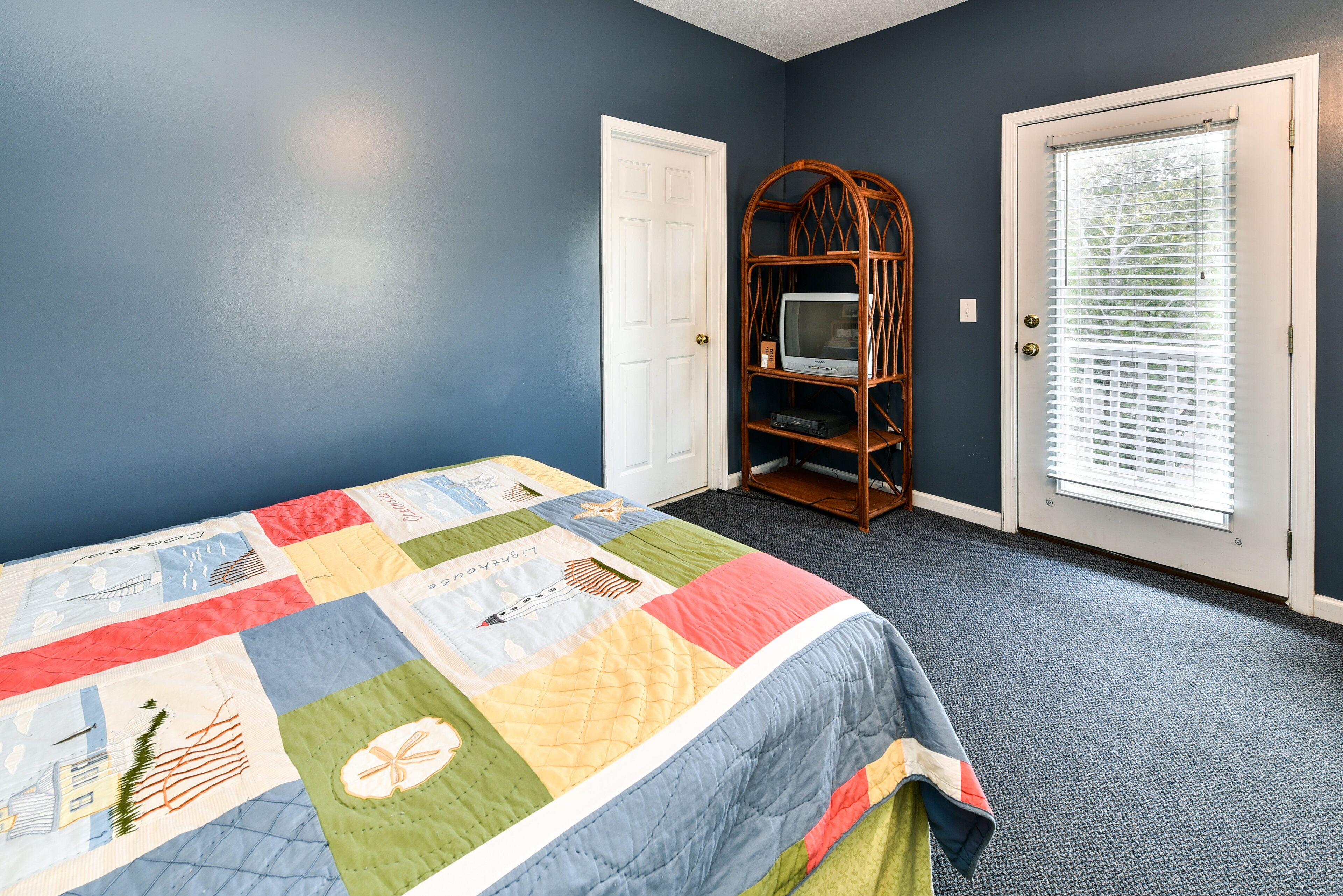A bedroom with a large bed, a television on a wooden stand, and a door with blinds.