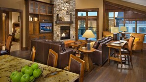 A spacious living room with a stone fireplace, leather sofas, a dining area with a table, and a large window offering a view. - Ski in, Ski out, luxury resort. Exceptional snow (Truckee)