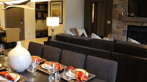 A modern living room with a dark sofa, a fireplace, and a dining area set with plates, glasses, and a vase. - Ski in, Ski out, luxury resort. Exceptional snow (Truckee)