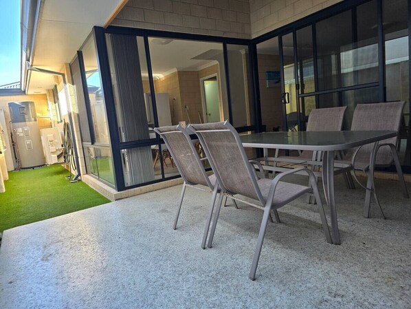 An outdoor patio with a table and chairs, a glass door leading to a room, and a small lawn area.