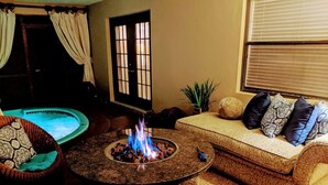 A cozy living room with a stone fire pit, a pool, a sofa with patterned cushions, and a potted plant. - Stunning Indoor & Outdoor Living near Beach and Shopping. Close to Boca Raton (Deerfield Beach)
