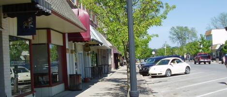 A sidewalk with a street lamp, storefronts, and parked cars.