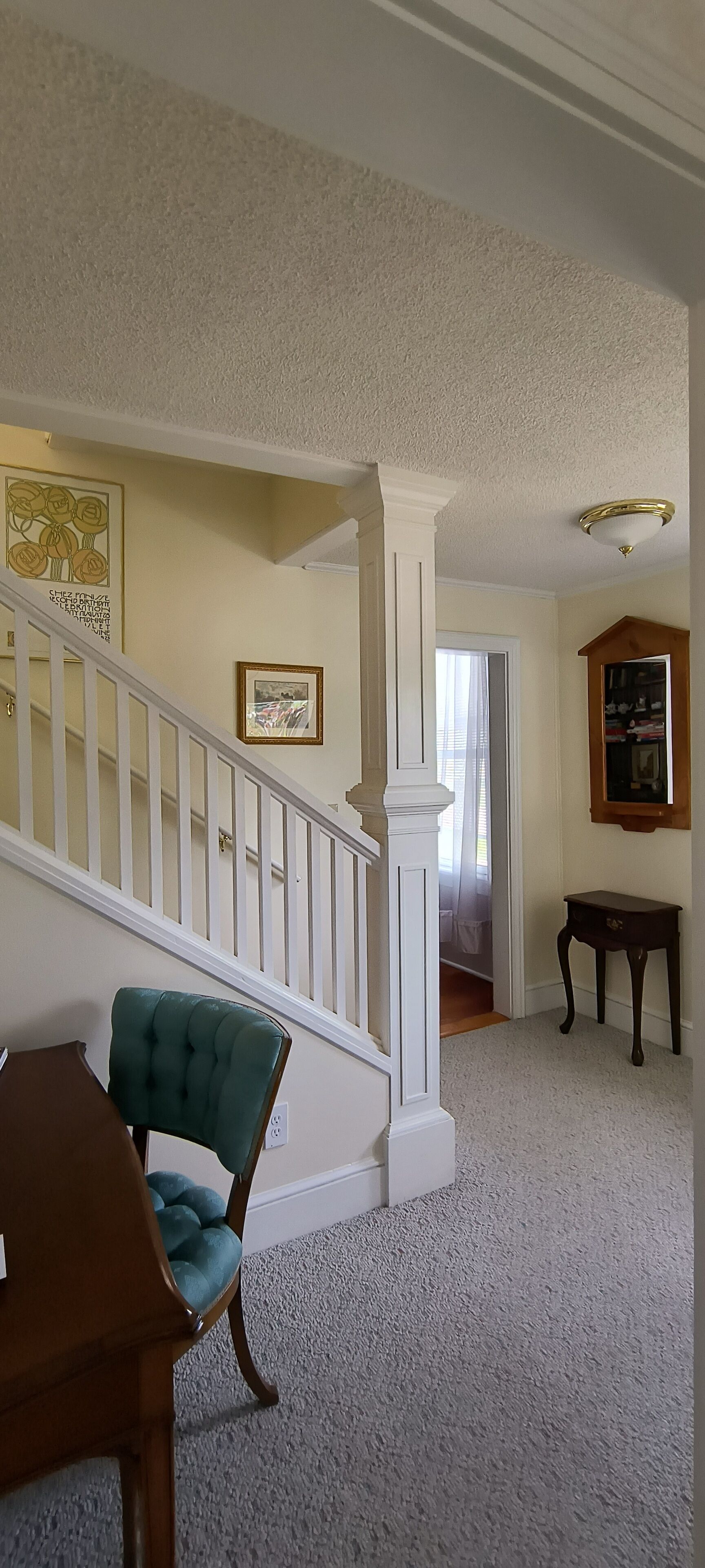 Un escalier avec des rampes blanches mène au deuxième étage. Un fauteuil vert, recouvert de tissu, est placé près du bas de l’escalier.