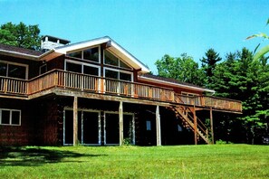 A large, two-story house with a wooden deck and a staircase leading to a second-floor balcony. - Hickory Hill Mountaintop charming family friendly quiet very private lake view (Bolton Landing)