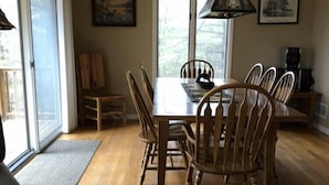 A dining area with a wooden table and chairs, large windows, and a hanging light fixture. - Hickory Hill Mountaintop charming family friendly quiet very private lake view (Bolton Landing)