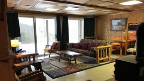 A cozy living room with a wooden floor, a patterned sofa, a coffee table, and a fireplace. - Hickory Hill Mountaintop charming family friendly quiet very private lake view (Bolton Landing)