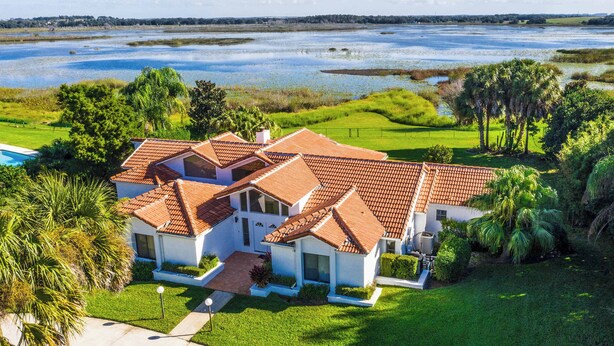 A large, modern house with a red-tiled roof, surrounded by lush greenery and a body of water. - SWISS 06 - Lake Sumner (Clermont)
