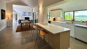 A modern kitchen with a large island, bar stools, and a view of greenery through the window. - SWISS 06 - Lake Sumner (Clermont)