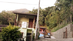 Um pequeno edifício térreo com varanda, uma placa e uma escadaria que leva à porta.