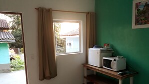 Quarto com porta de correr para uma varanda, uma pequena mesa com micro-ondas e torradeira, e uma parede verde.