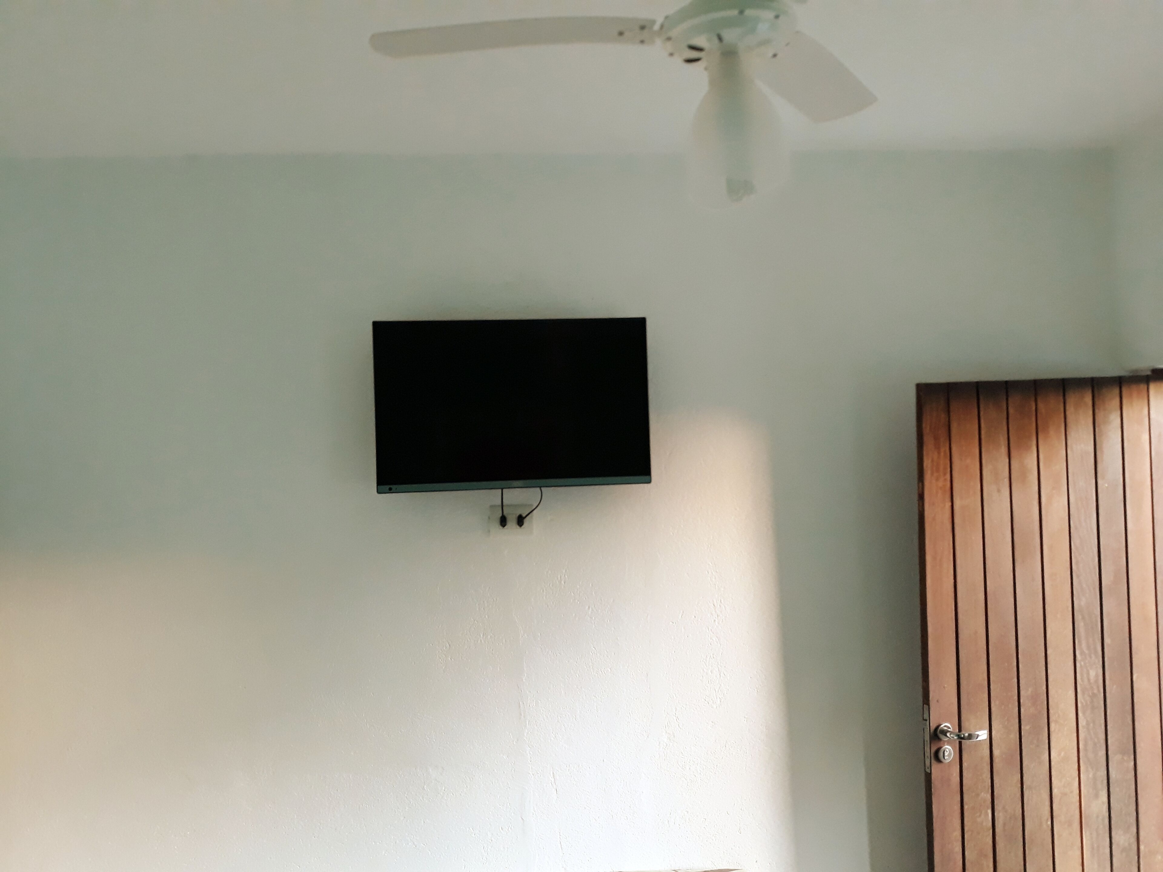 Una habitación con ventilador de techo, televisor de pantalla plana montado y puerta de madera.
