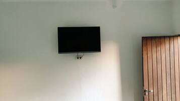Una habitación con ventilador de techo, televisor de pantalla plana montado y puerta de madera.