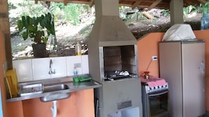 Uma cozinha ao ar livre com pia, churrasqueira e geladeira.