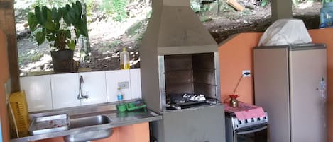 Una cocina exterior con pileta, parrilla y refrigerador.