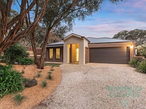 A modern house with a gravel driveway, a garage, and a landscaped garden with trees and shrubs.