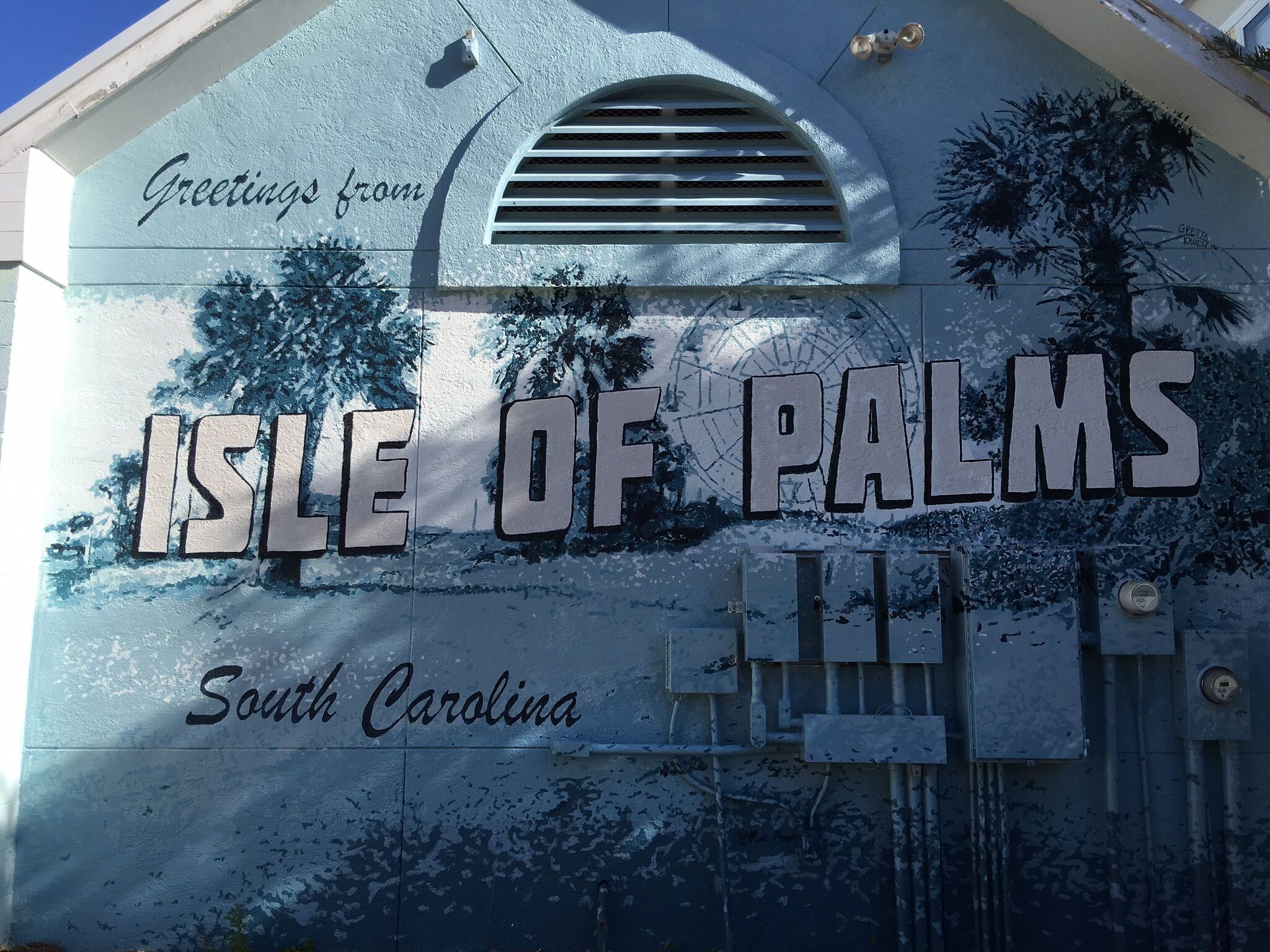 A sign with the text "Greetings from Isle of Palms, South Carolina" and a depiction of palm trees.
