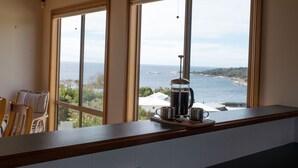 Una cocina con vistas al mar a través de amplios ventanales, una cafetera y una silla.