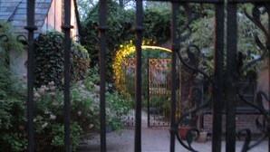 Um jardim com portão de metal, paredes de tijolo e vegetação.