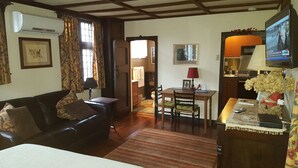 Uma sala de estar acolhedora com um sofá de couro, uma mesa de jantar com cadeiras e uma televisão sobre um móvel.