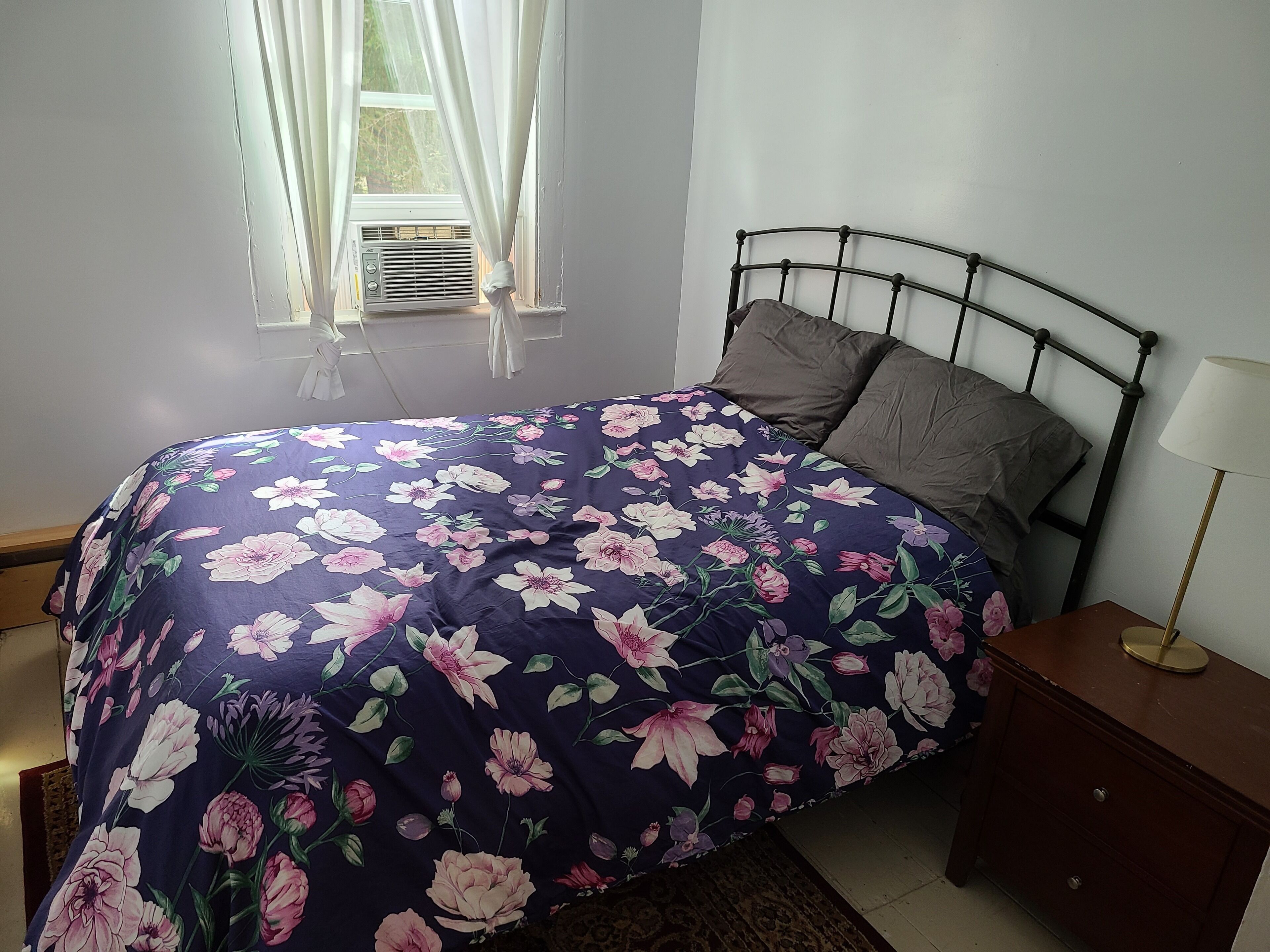 Une chambre à coucher avec un lit, une table de chevet, une lampe et une fenêtre avec des rideaux.