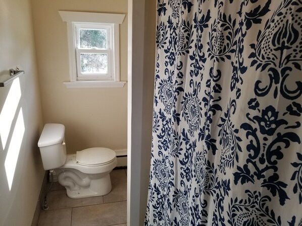 A bathroom with a toilet, a window, and a shower curtain with a floral pattern. - Victorian Catskill House w/ Game Room, Fire Pit, and Strong Wi-Fi (Lexington)
