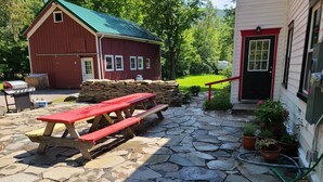 Eine Steinterrasse mit Picknicktischen, ein rotes Bauernhaus und ein Haus mit roter Tür.