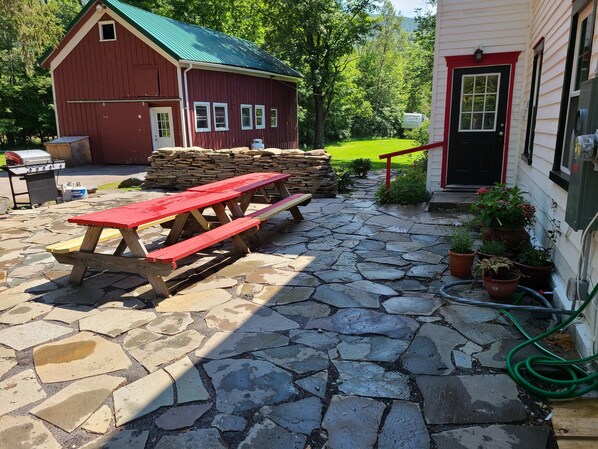 A stone patio with picnic tables, a red barn, and a house with a red door.