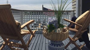 Eine Holzterrasse mit zwei Korbstühlen und einem Tisch, einer dekorativen Vase mit Blumen und einer amerikanischen Flagge im Hintergrund.