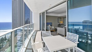 En balkon med havudsigt, et spiseområde med hvide møbler og en stue med sofa og tv.