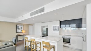 Et moderne køkken med en central ø, barstole, et spiseområde med en sofa og et stort vindue, der giver naturligt lys.
