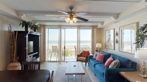 A living room with a TV, a sofa, a coffee table, and a balcony with a view of the beach. - Beachfront Luxury 1 BR Condo - 3 Oceanfront Pools (Tybee Island)