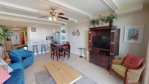 Uma sala de estar ampla com uma mesa de centro de madeira, um rack para TV e uma área de jantar, com uma cozinha ao fundo.