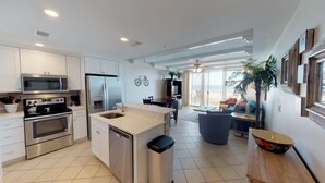 A modern kitchen with built-in appliances, a dining area with a view, and a living space with a sofa and a plant. - Beachfront Luxury 1 BR Condo - 3 Oceanfront Pools (Tybee Island)