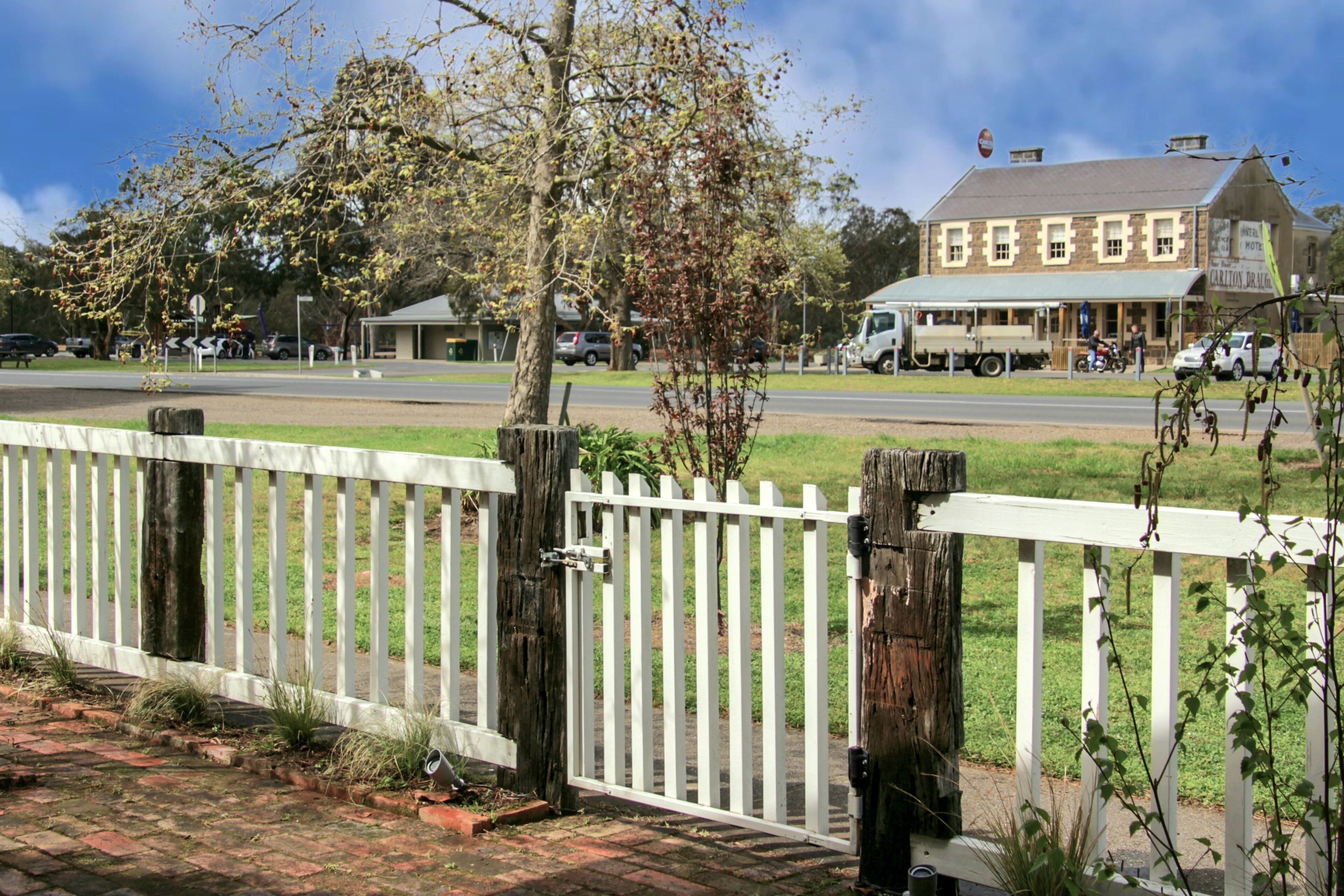 A white picket fence, a brick pathway, and a building with a sign that reads "Carlitos de Urquijo."
