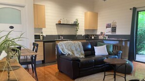 Ein modernes Wohnzimmer mit einer schwarzen Ledersofa, einem Holzessttisch und einer Küchenzeile mit Holzschränken und einer schwarzen Arbeitsplatte.