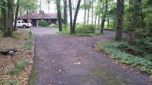 A forested area with a paved driveway leading to a building with a dark roof and a white truck parked nearby. - Rustic Mountain Lakefront Cottage  (Scottsboro)