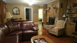 A living room with a brown leather sofa, a patterned armchair, a coffee table with magazines, a fireplace, and a wooden cabinet. - Rustic Mountain Lakefront Cottage  (Scottsboro)