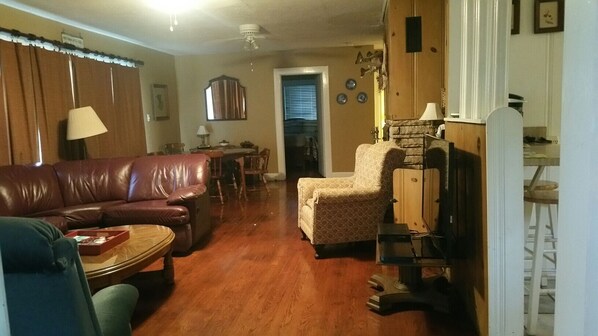 A living room with a leather sofa, patterned armchair, and a small table. There is a wooden cabinet and a lamp on a stand.