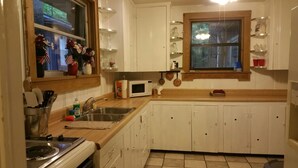 A kitchen with white cabinets, a microwave, a sink, and a window with flowers. - Rustic Mountain Lakefront Cottage  (Scottsboro)