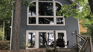 Une maison à deux étages, dotée d’un mur en pierre et d’un escalier en bois menant à une terrasse.