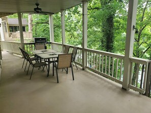 Une terrasse couverte, dotée d’une table et de chaises, entourée d’une balustrade blanche, et offrant une vue sur un paysage verdoyant luxuriant.