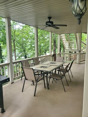 Un espace extérieur abrité, aménagé pour prendre les repas, avec une table et des chaises, un ventilateur de plafond et une vue sur les arbres et un escalier.