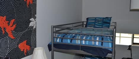 A bunk bed with a blue and white striped bedspread, a white lamp on a wooden table, and a wall with a black and red abstract design.