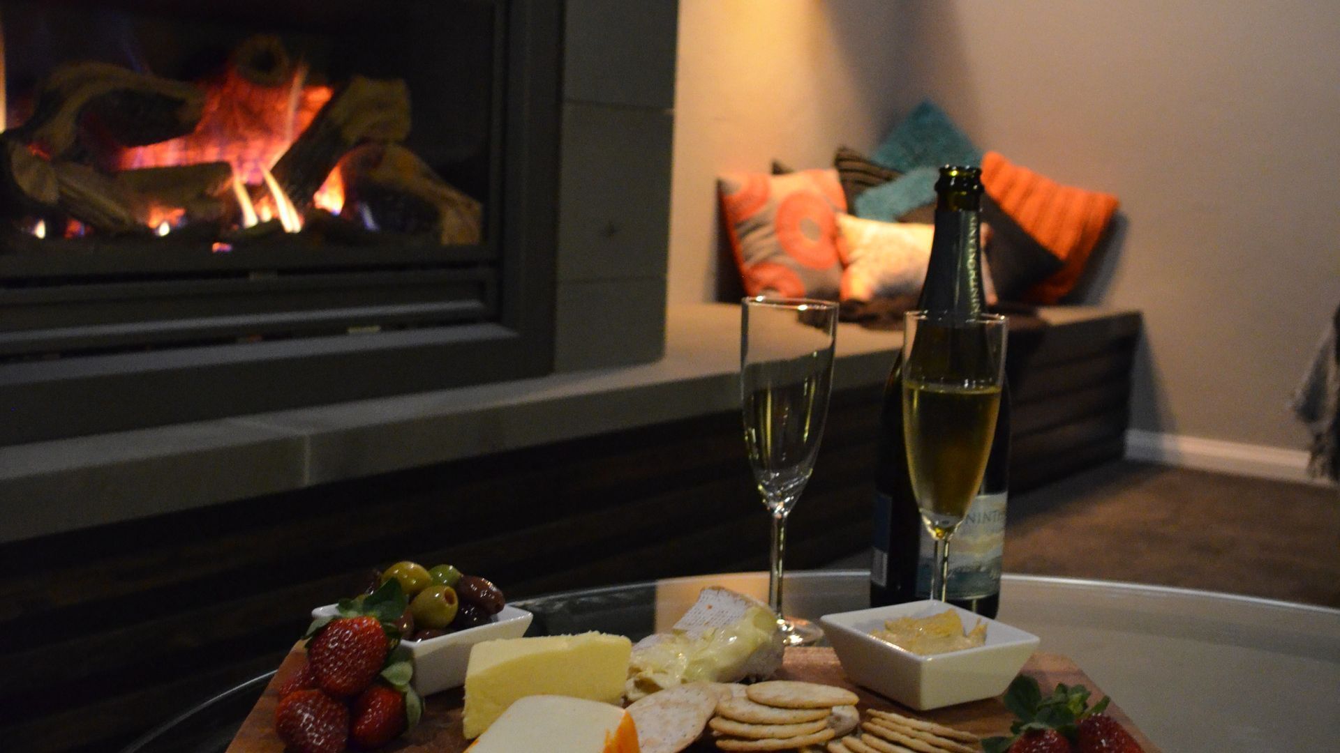 Une pièce chaleureuse avec une cheminée, une table garnie de collations et des verres de vin.