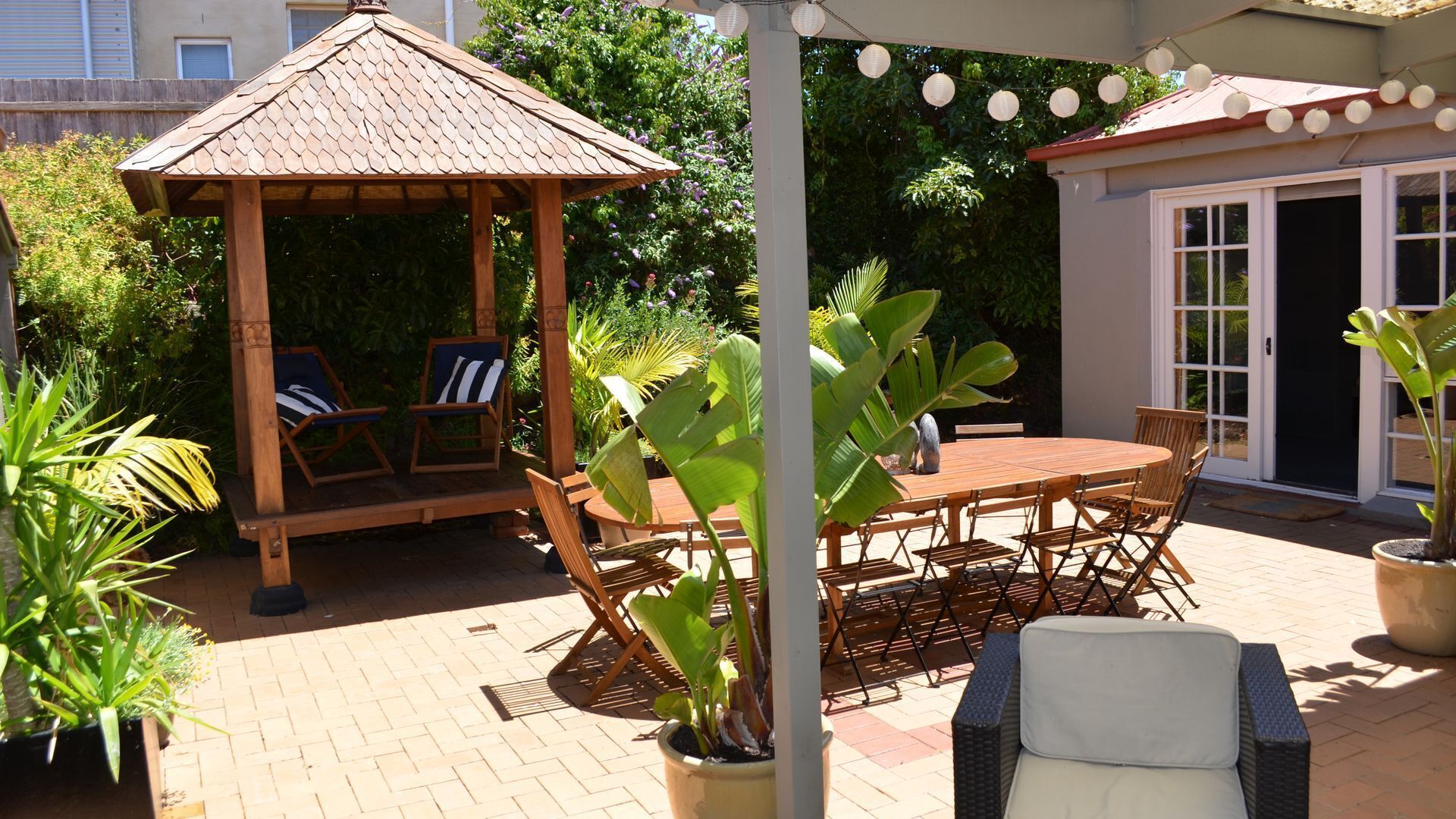 A patio with a wooden gazebo, outdoor seating, and a dining table.