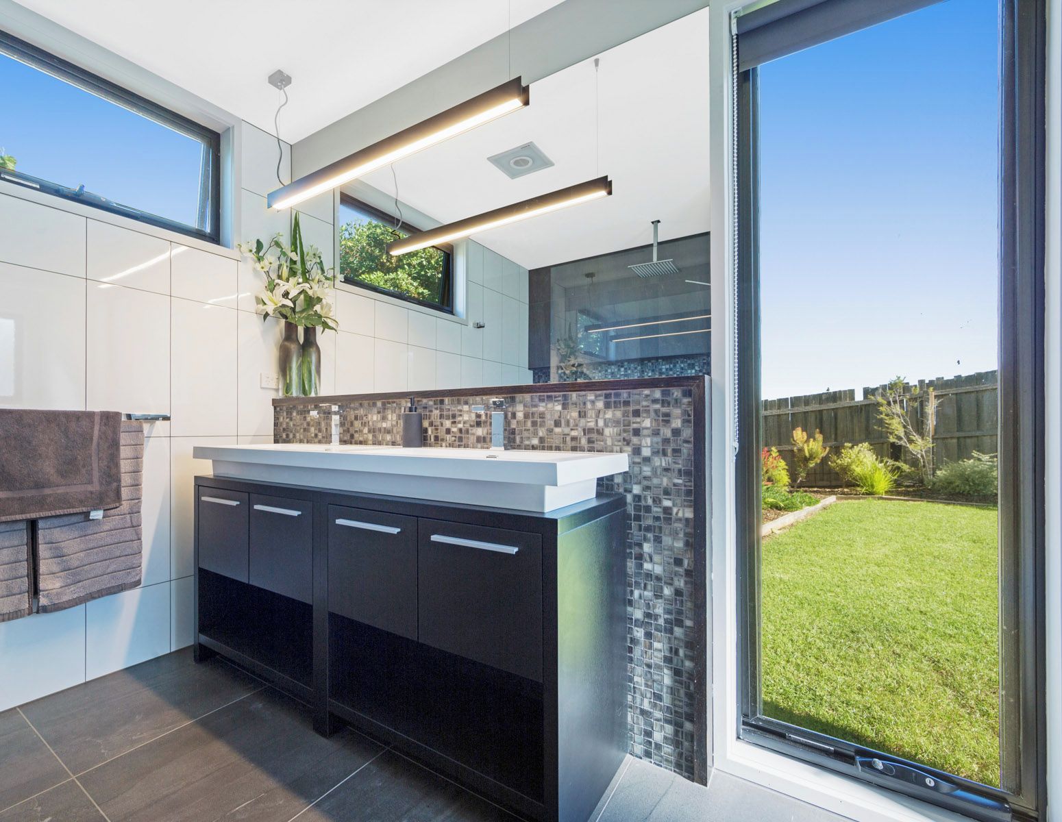A modern kitchen with a large island, white tiles, and a view of a well-maintained garden.