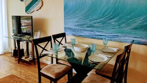 A dining area with a glass table, chairs, and a large wave painting on the wall. - Unobstructed ocean view 2Br/2Ba - upscale at a budget price (Kihei)