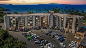 A multi-story hotel with a parking lot and a view of the ocean. - Unobstructed ocean view 2Br/2Ba - upscale at a budget price (Kihei)