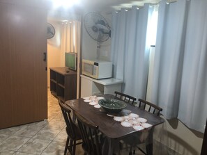 Een eethoek met een houten tafel, stoelen, een magnetron en een ventilator.